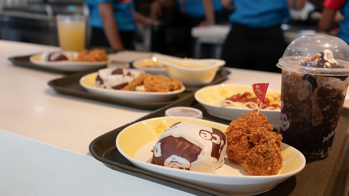 トレイに載ったフライドチキン、紙に包まれたライス、パスタ、チョコレートサンデーが並ぶ店内のカウンター
