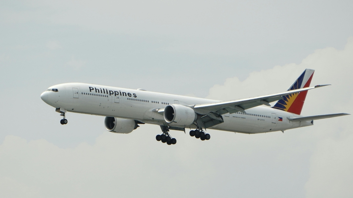 青空を背景に、白い機体に黒文字でPhilippinesと書かれたフィリピン航空の旅客機がギアを出して着陸体制で飛行する