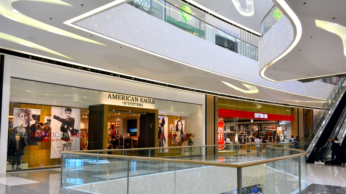 吹き抜けのあるショッピングモールの内観。手前にガラスの手すりがあり、その先に「AMERICAN EAGLE OUTFITTERS」と「COTTON ON」の店舗、そして右側にエスカレーターが見える。