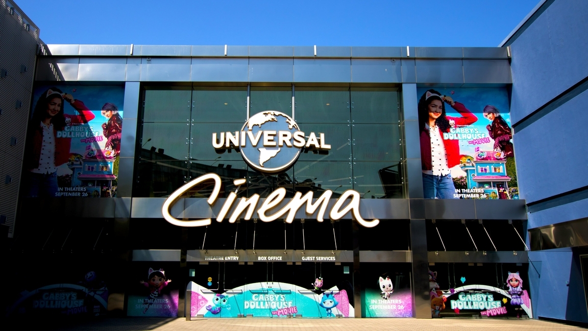 ガラス張りの壁に「UNIVERSAL Cinema」のロゴが光る映画館の入り口。壁面にはアニメキャラクターの大きなポスターが貼られ、下部の自動ドア付近にもカラフルな作品広告が並んでいる近代的な外観です
