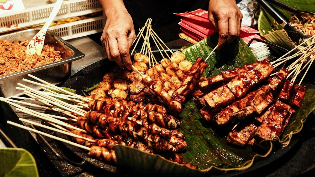 バナナの葉を敷いた大きなトレイに、タレの塗られた焼き鳥や串刺しの厚揚げが山積みになっている。背後では調理担当者が串を整理している