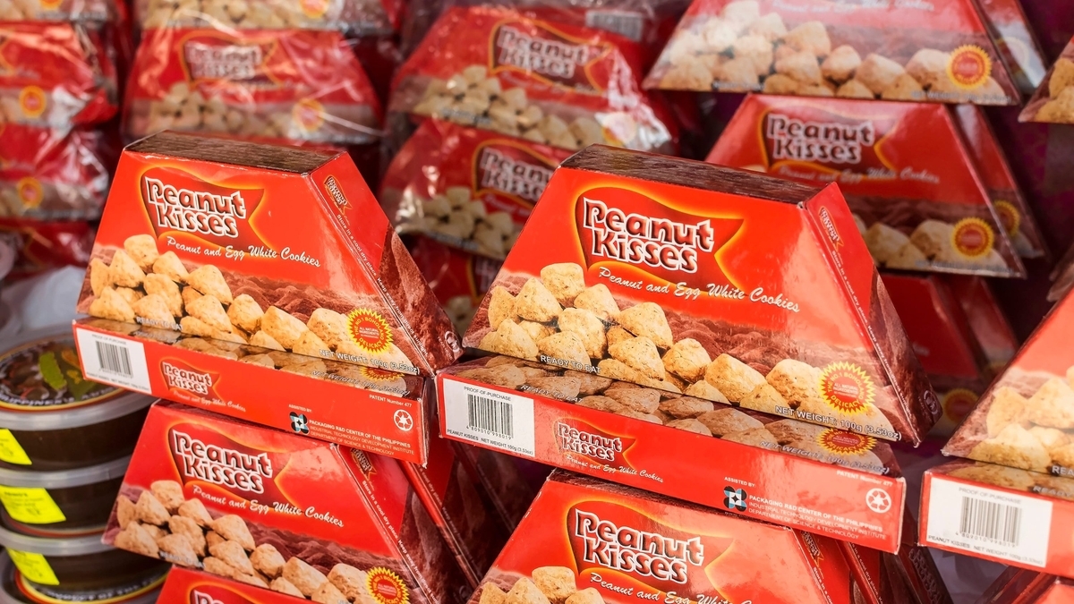 赤い台形型のパッケージに入った「Peanut Kisses」というお菓子が、棚に大量に積み上げられています。表面には、山のように盛られた茶色のクッキーのイラストが描かれています。