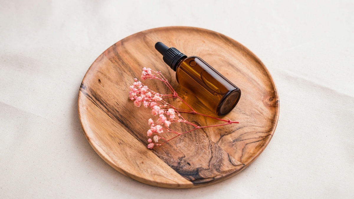 木製の丸いトレイの上に、黒いキャップがついた茶色の遮光瓶と、ピンク色の小さなかすみ草のドライフラワーが添えられている様子