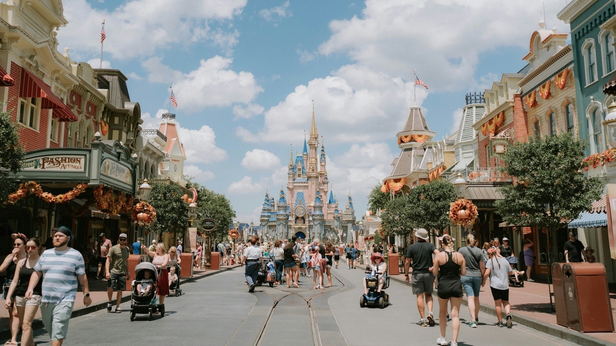 晴天のディズニーワールドのメインストリートUSA。道の両側にクラシカルな建物が並び、奥には青とゴールドの装飾が施されたシンデレラ城がそびえ立ち、通りを多くの人々が行き交っている
