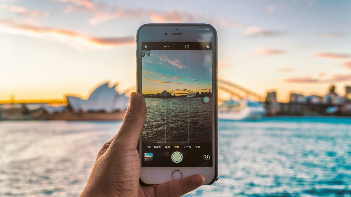 夕暮れの空を背景に、スマートフォンの画面に写るシドニー・オペラハウスとハーバーブリッジの景色