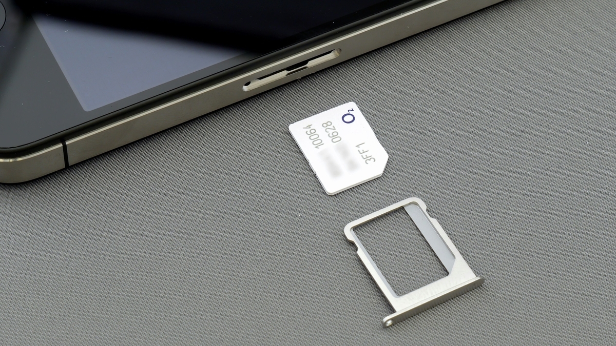 スマートフォンの側面にあるトレイから取り出された、白いO2ブランドのSIMカードとその金属製トレイ