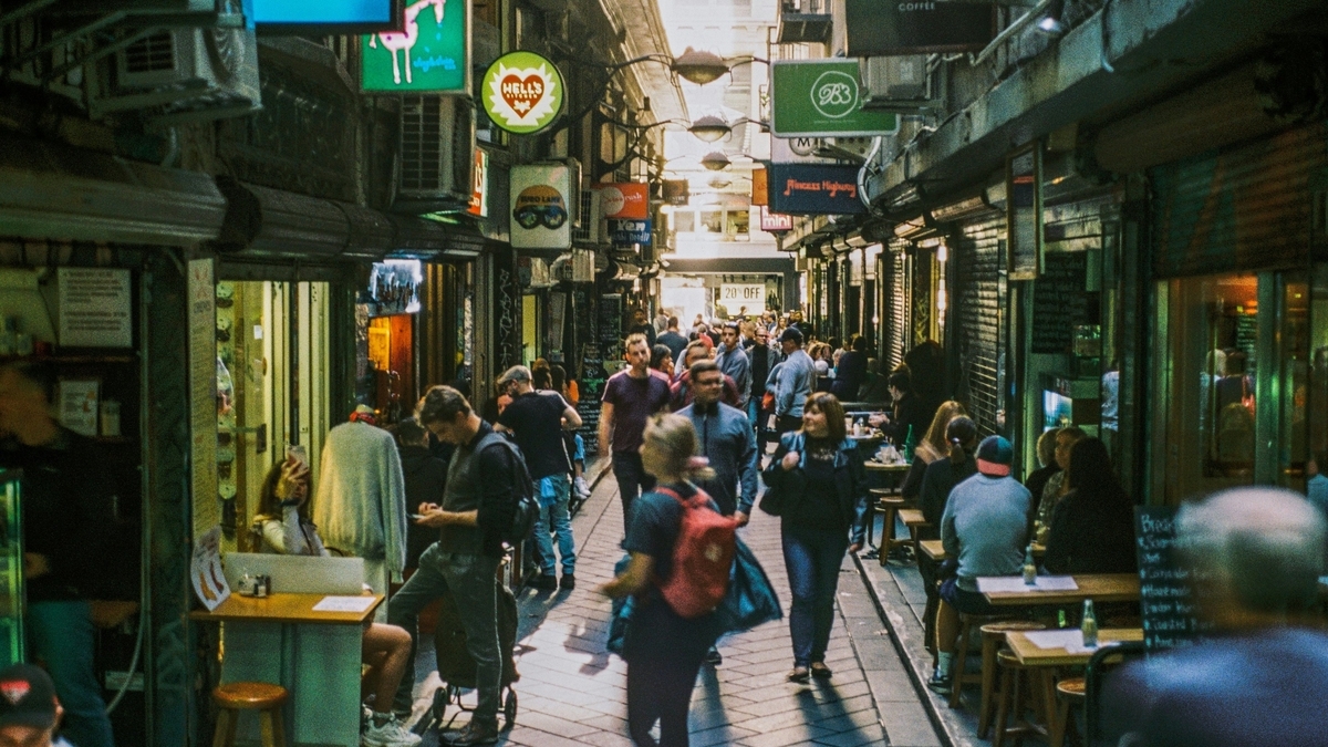 飲食店が立ち並び、多くの人々が行き交う狭い路地風の通りと、頭上に掲げられた複数の看板