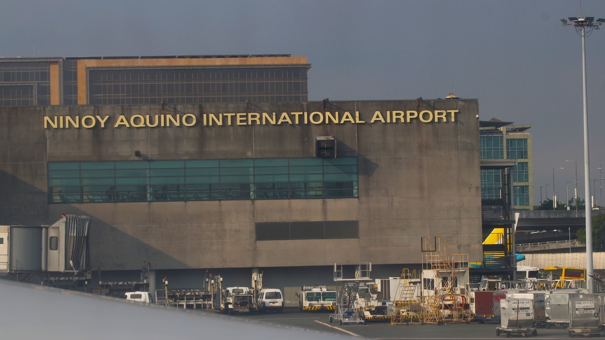 青空の下に佇むニノイ・アキノ国際空港の外観と、手前の敷地に並んでいる複数の白い空港作業用車両