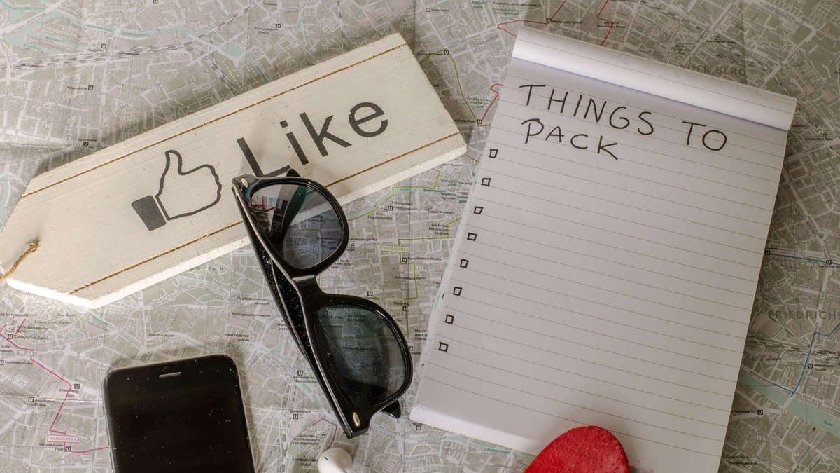 「THINGS TO PACK」と書かれたメモ帳、サングラス、スマートフォン、いいねのマークの看板が広げられた地図の上に置かれている様子