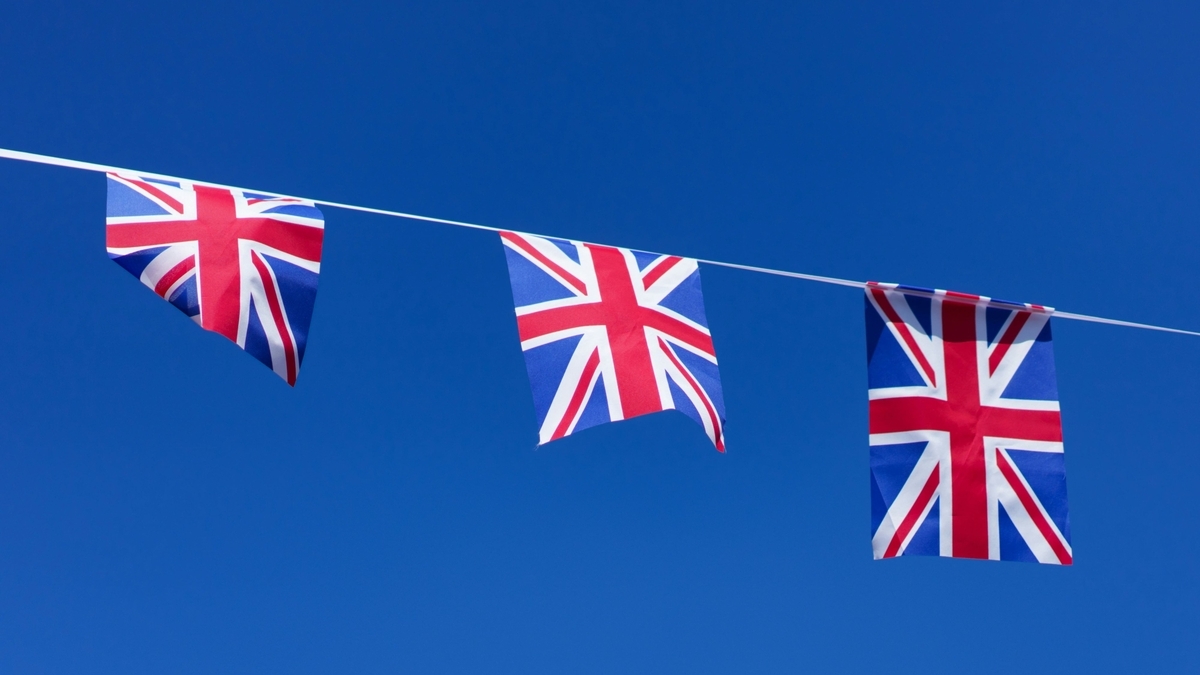 青空を背景に、白いロープに等間隔で吊るされて並んでいる3枚のイギリス国旗の万国旗