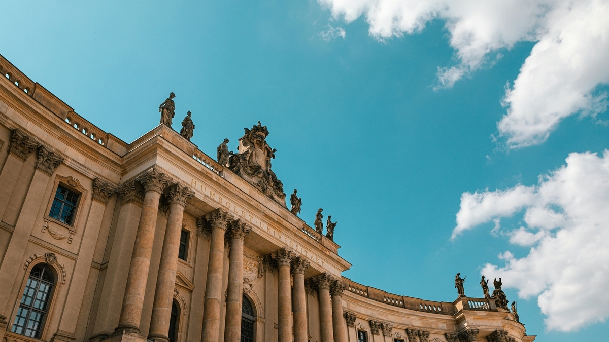 青空を背景に、上部に多数の彫刻が飾られ「HUMBOLDT-UNIVERSITAET」と刻まれた歴史的な建物の外観を斜め下から見上げた様子