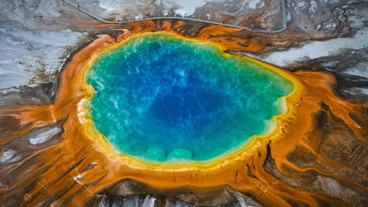 中央に鮮やかな青色の大きな熱水泉があり、その周囲を黄緑色やオレンジ色の同心円状の地表が囲んでいる、上空から見下ろした景色