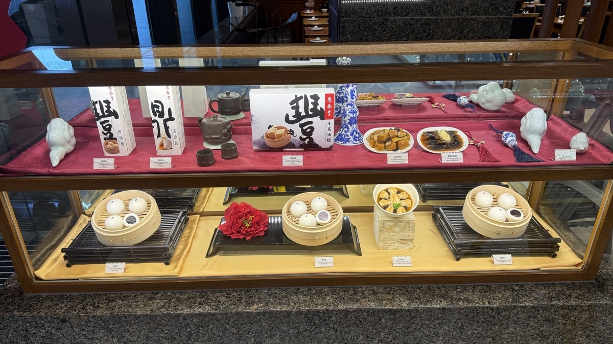 ガラス張りのショーケース内にディスプレイされた、せいろに入った中華まんの食品サンプルや、箱に入った土産物、茶器などが2段にわたって並べられている様子
