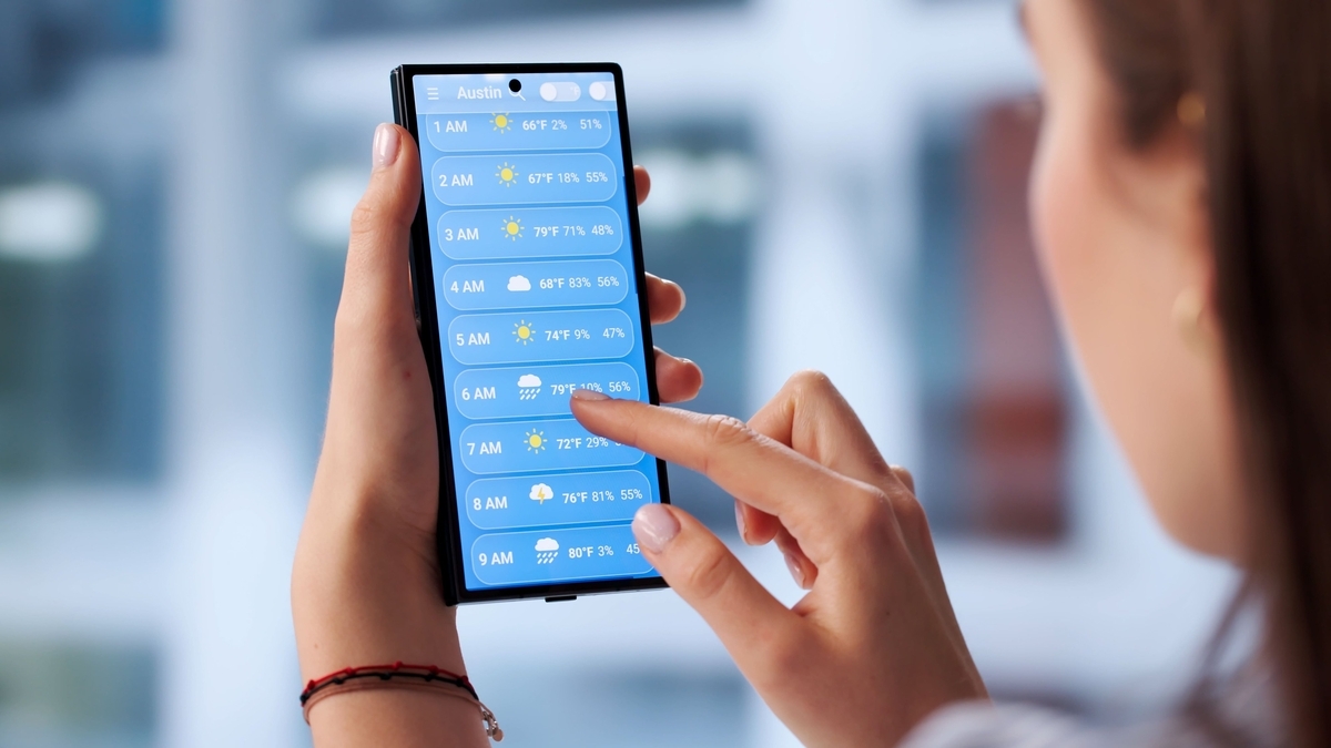 女性がスマートフォンを持ち、画面に表示された時間ごとの天気予報のアプリを指で操作している手元のアップ