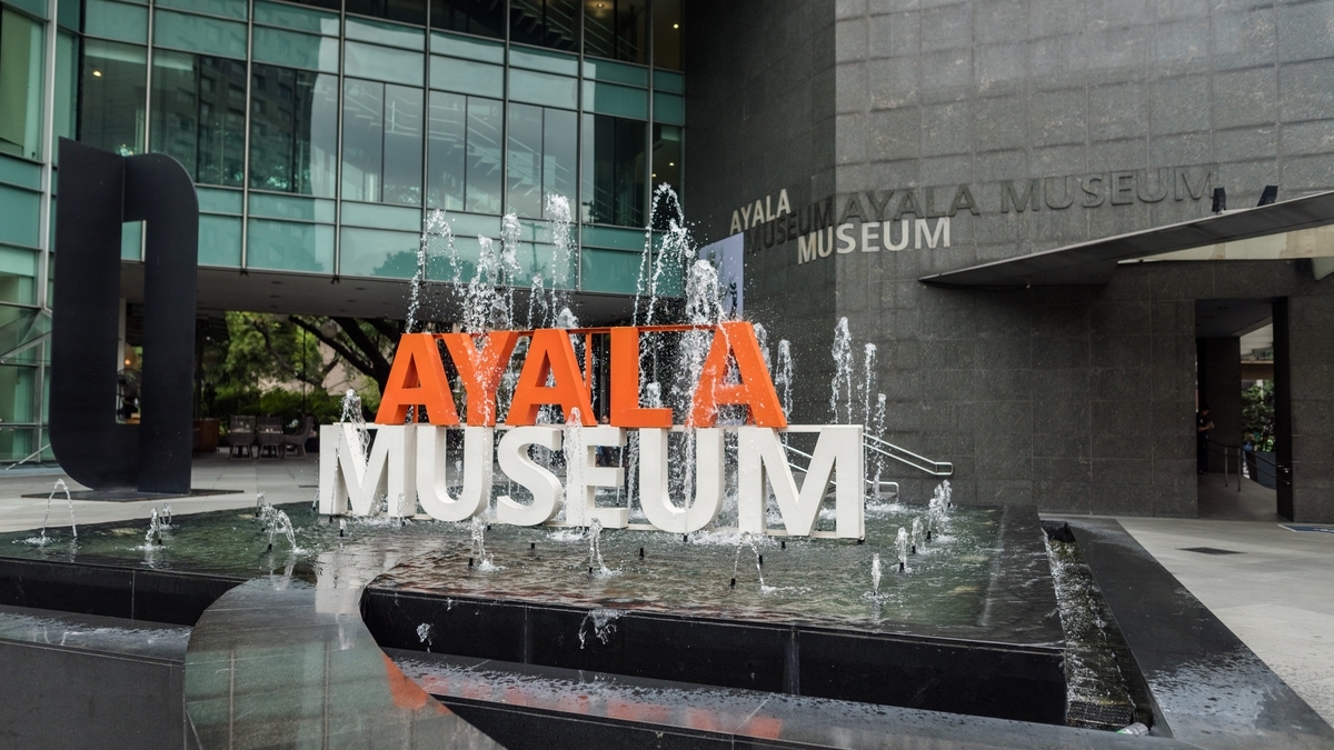 水が吹き出す四角い噴水の中に設置された、オレンジと白の文字で構成されたAYALA MUSEUMの立体ロゴ
