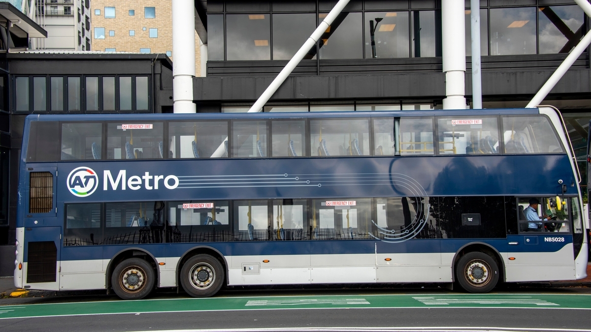 側面に「AT Metro」のロゴと白い曲線デザインが施された、濃紺とシルバーのツートンカラーの2階建て路線バスを真横から捉えた写真