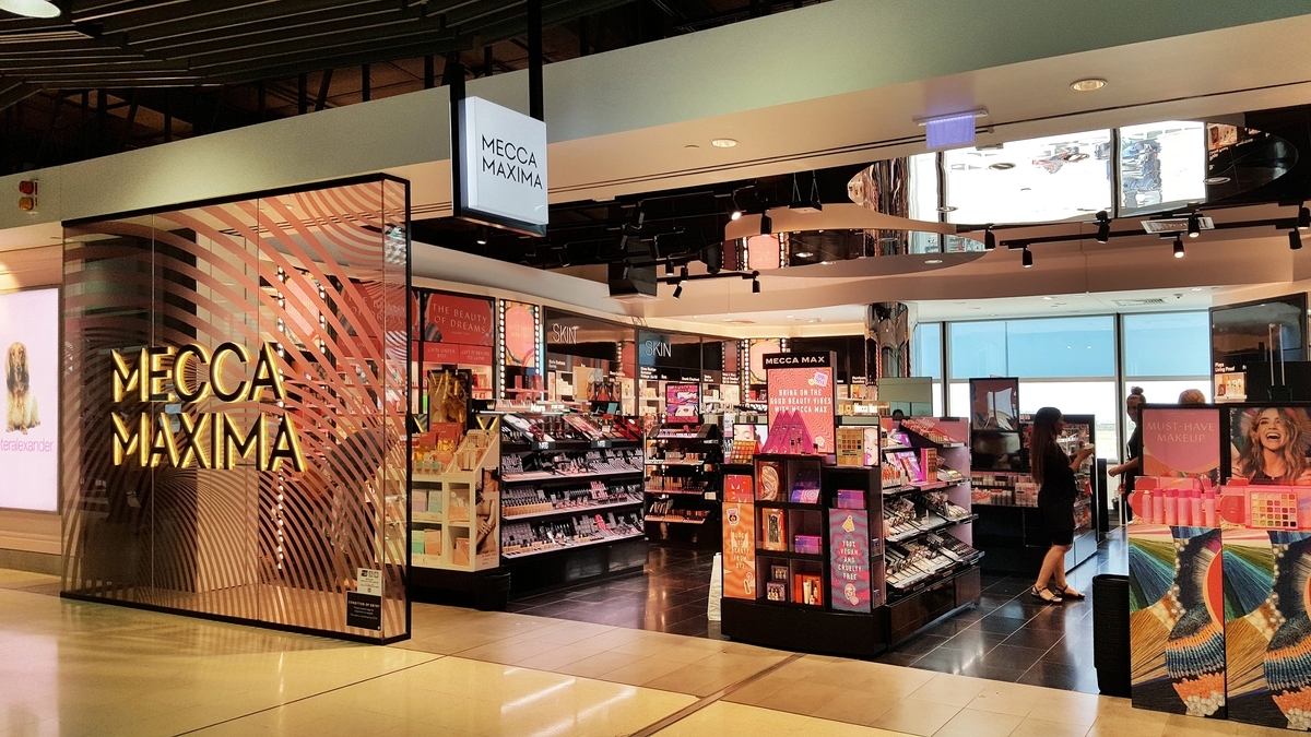 「MECCA MAXIMA」という看板とロゴが設置された、化粧品やスキンケア商品が多数陳列されている明るい店舗の内観