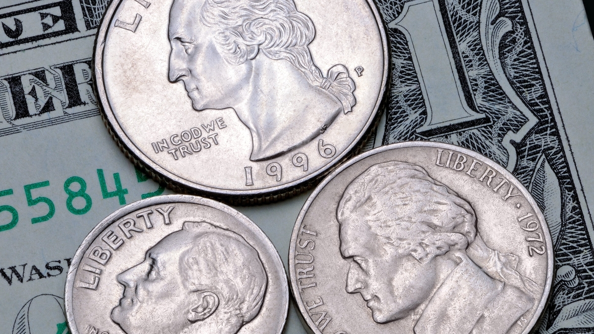1ドル札などの紙幣の上に、3枚の銀色の硬貨が重なるように置かれています。上部には1996年の刻印があるワシントンの横顔の硬貨があり、下部にも人物の横顔が刻まれた大小2枚の硬貨が並んでいます。