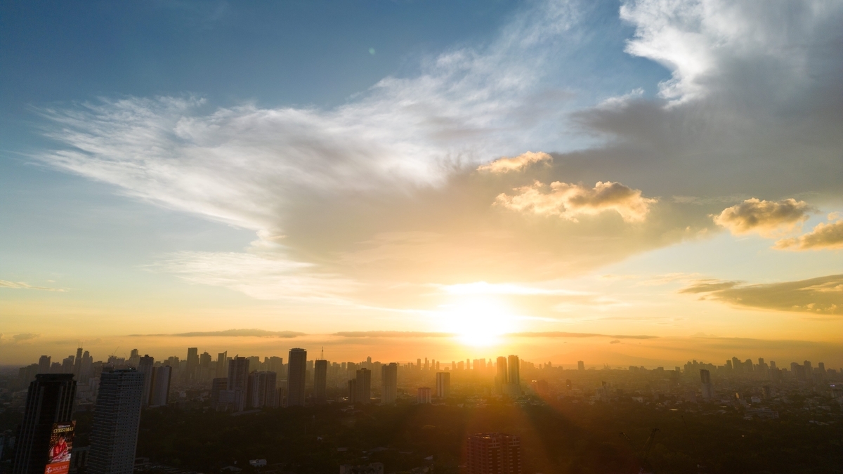 橙色に輝く夕日がビル群のシルエットと空一面の雲を照らす、街の全景。