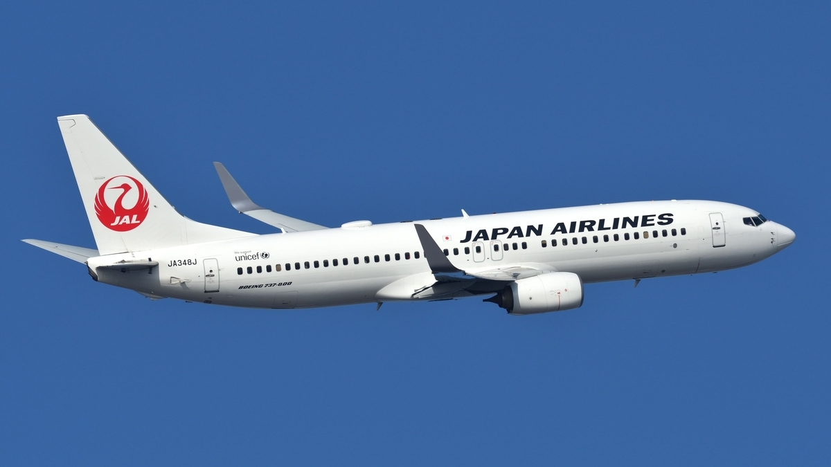 雲のない青空を背景に飛行している日本航空の旅客機で、白い機体の垂直尾翼には赤い鶴のマークが描かれ、胴体には黒い文字でJAPAN AIRLINESと記されています。   