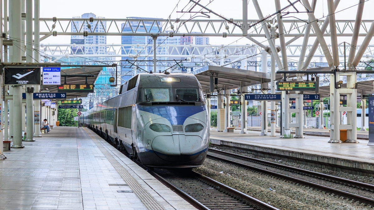 鉄骨の屋根と架線が張り巡らされた駅のホームに、青とグレーの塗装が施された流線型の特急列車が停車しています。ホームの上部には、時刻や行き先を示す電光掲示板が設置されています。   
