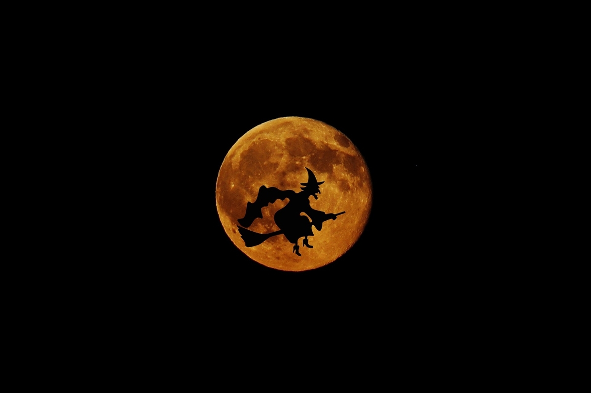 月を背後に、箒に乗って空を飛ぶ魔女の姿がシルエットとして映っている画像。