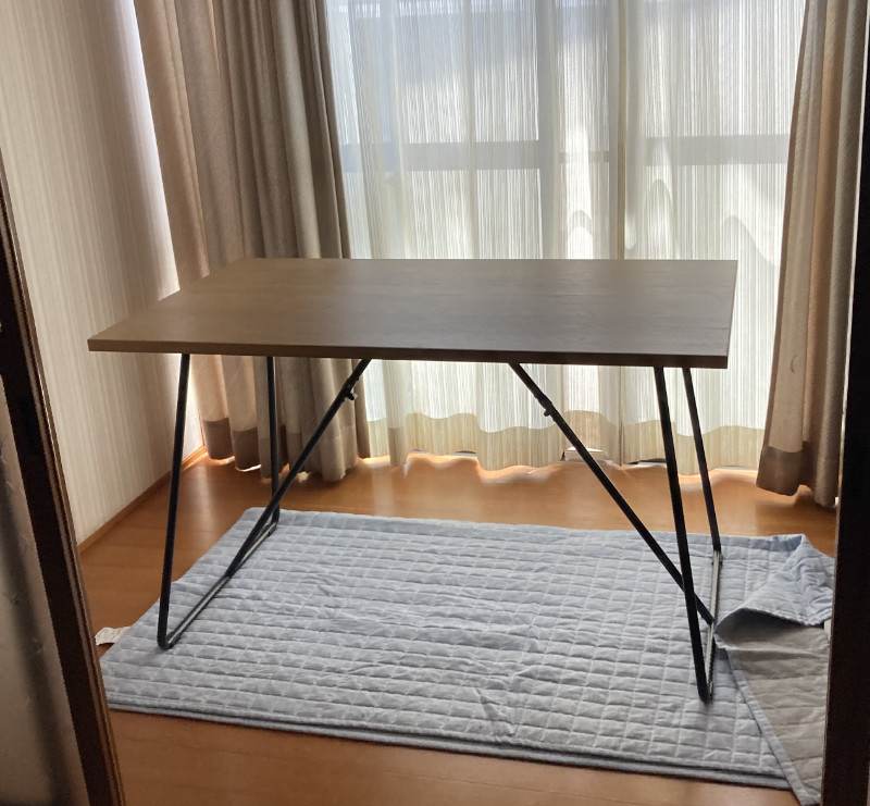 写真:部屋の広縁に置かれたテーブル。テーブルの下には半分に折りたたまれた水色のカーペットがある。