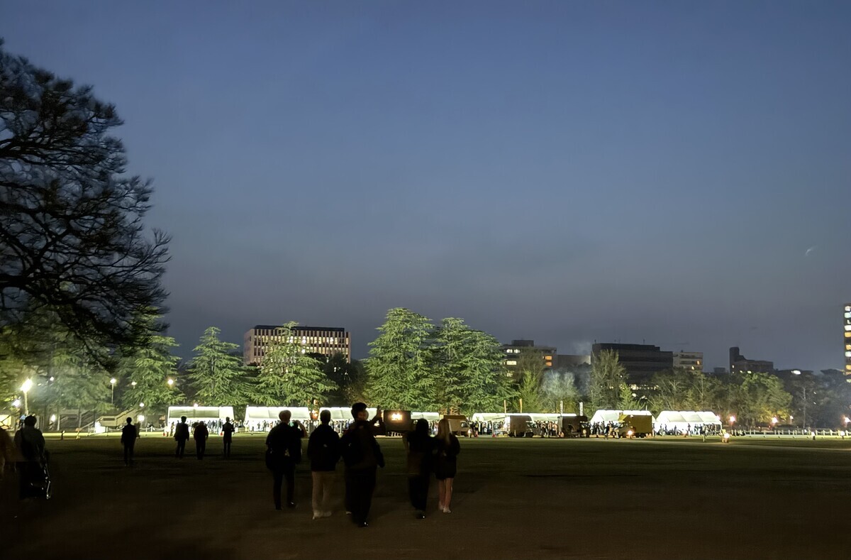 城山公園に入ったところ。向こうに見える白いテントはすべてオフィシャルパーティーのケータリングが並んでいるところ。その手前にキッチンカーが4〜5台並んでいる。さらに手前には、会場へ向かう人々が見える。