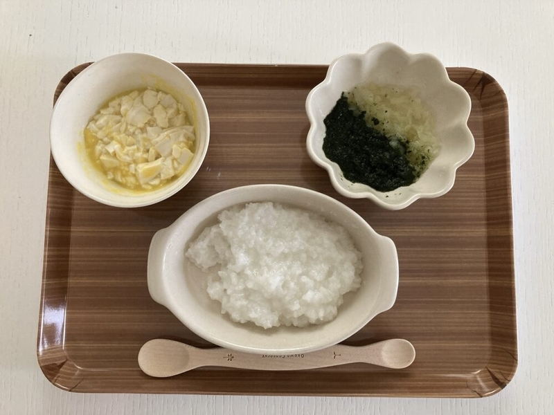 お盆の上に、小さい離乳食用のお粥とおかずが二つのっている。おかずは豆腐と刻み野菜。