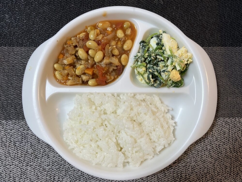 区切りがある白いプラスチックのお皿に、ご飯、チリコンカン、卵のサラダがのっている。