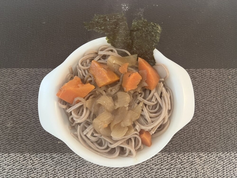 プラスチックの小皿にお蕎麦が入れられている。具は玉ねぎと人参で海苔が添えられている。