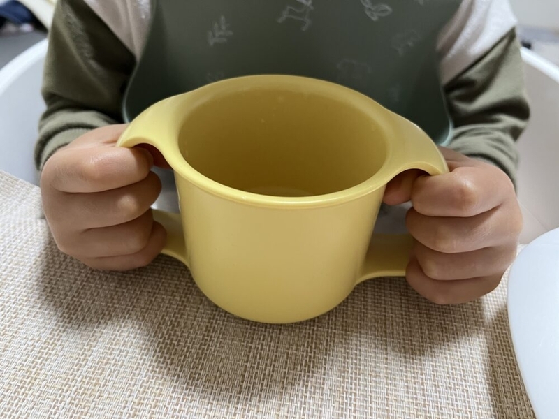 黄色いマグカップを子供が両手で持っている。