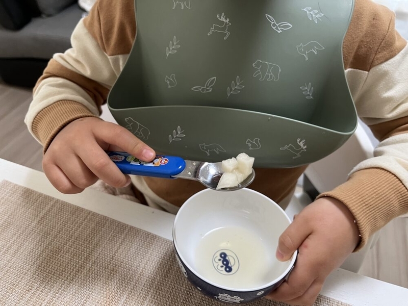 子供がスプーンを持って大根を食べている。反対の手にはアンパンマンのお茶碗。