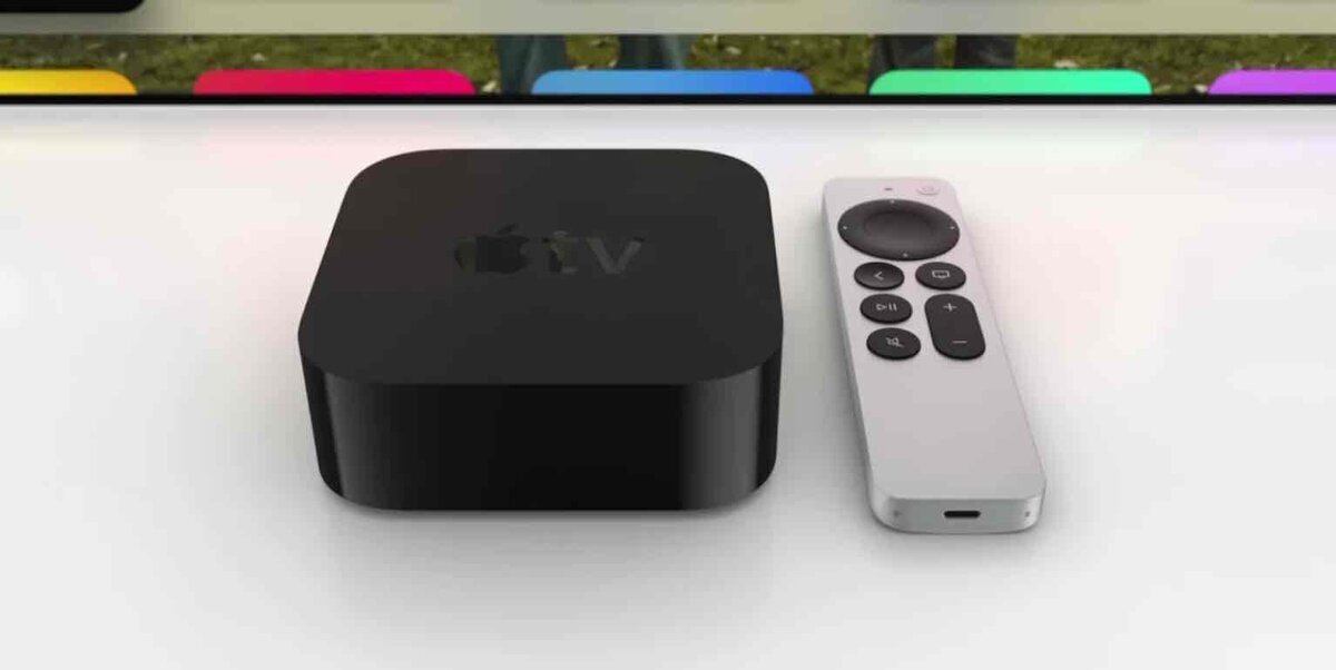 Apple TV 4K本体とSiri Remoteが並んで置かれている。黒いApple TVの上にはAppleロゴが刻まれ、背後にはテレビ画面のカラフルな映像がぼんやりと映っている。