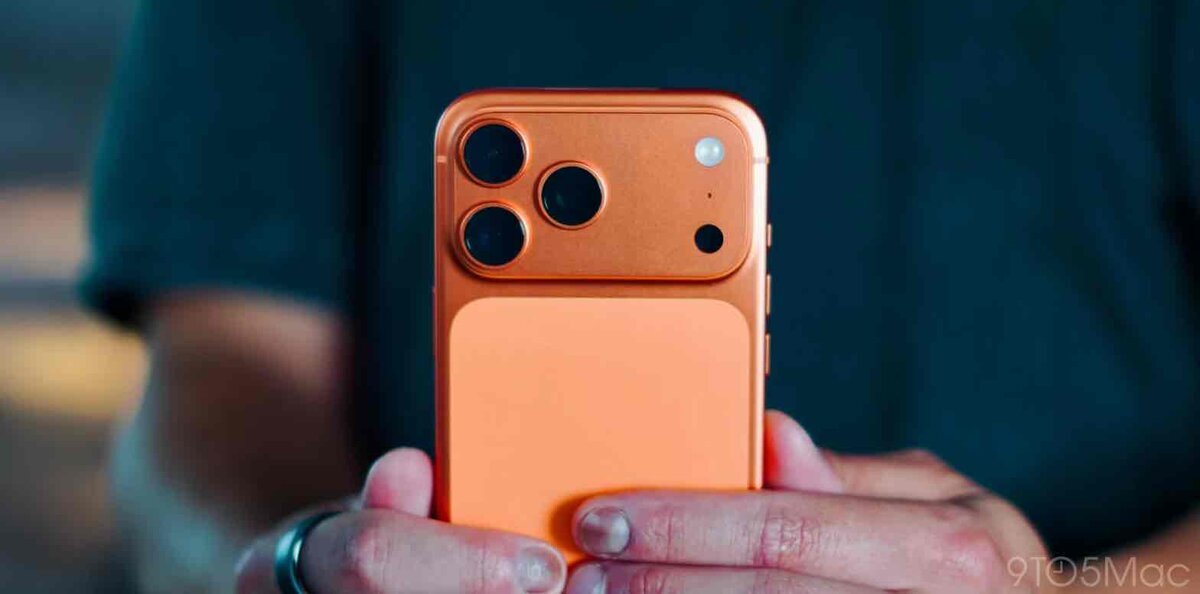 オレンジ色の試作デザイン風スマートフォン背面。上部に3眼カメラとフラッシュを備えた角丸の長方形パネルがあり、その下に質感の異なる大きな背面パネルが続く2トーン構成を手に持っている様子