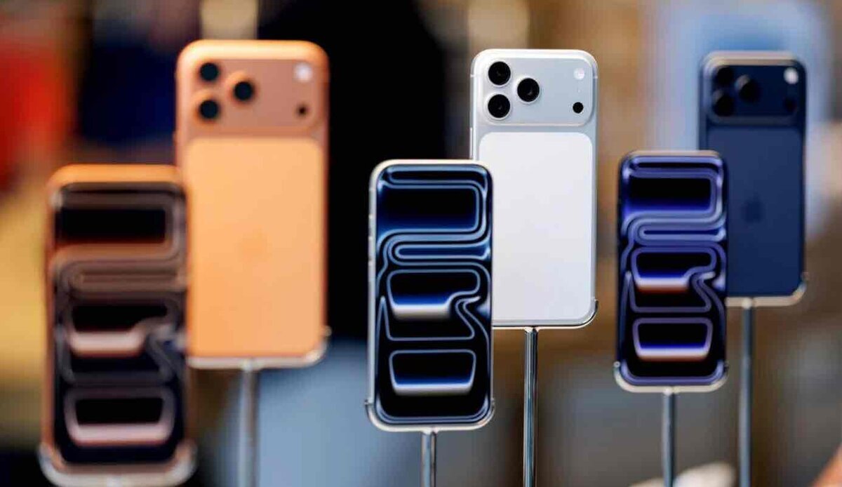 Apple Storeに展示された複数のiPhone。オレンジ、ホワイト、ネイビーなどのカラーが並び、背面カメラのデザインや前面ディスプレイがライトに照らされて強調されている様子