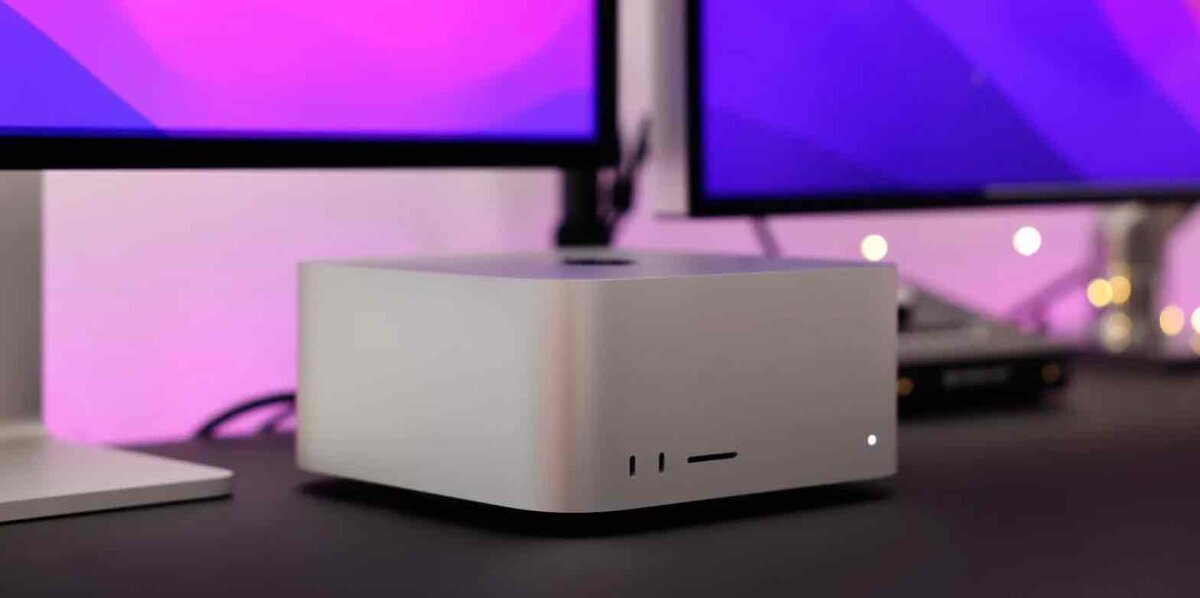 Mac Studio本体のクローズアップ。 前面にはUSB-CポートとSDカードスロットが並び、周囲にはピンクと紫が混ざった柔らかい照明が反射している。背後には複数の外部ディスプレイが映り、デスク上で使用されている様子がわかる