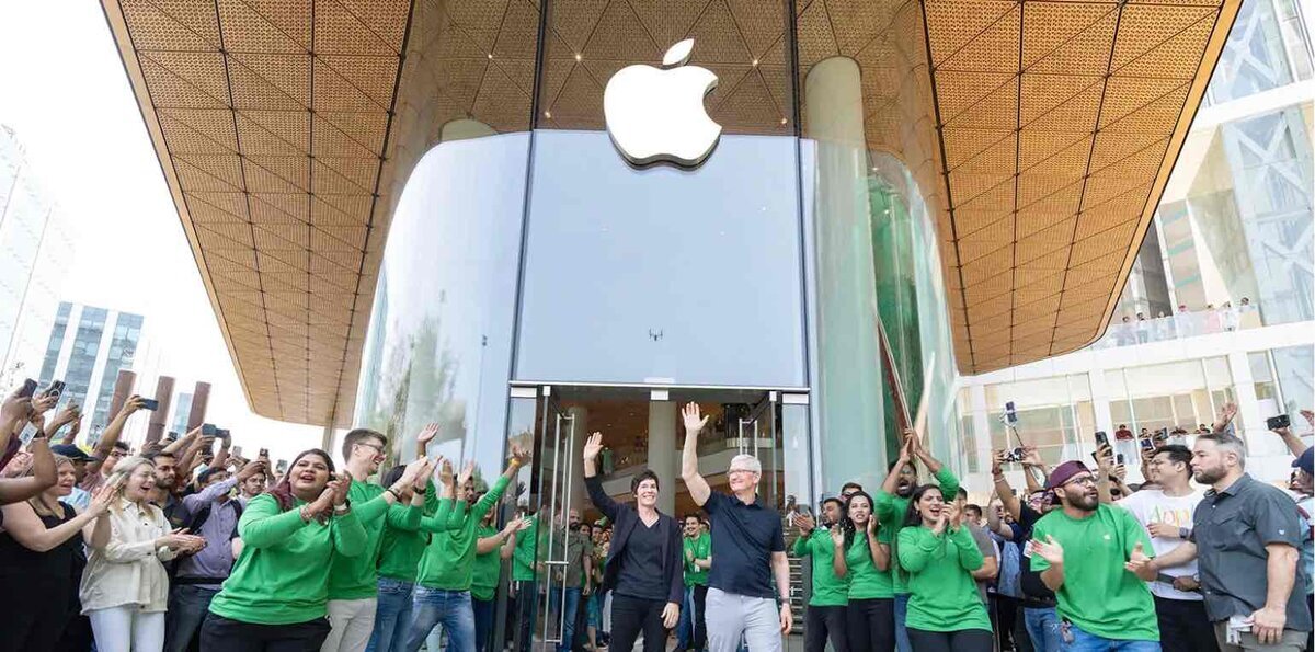 Apple Storeのエントランス前で、多くのスタッフと来店客が拍手しながら歓迎している様子。中央ではティム・クックらが笑顔で手を振り、新店舗オープンの高揚感が伝わる