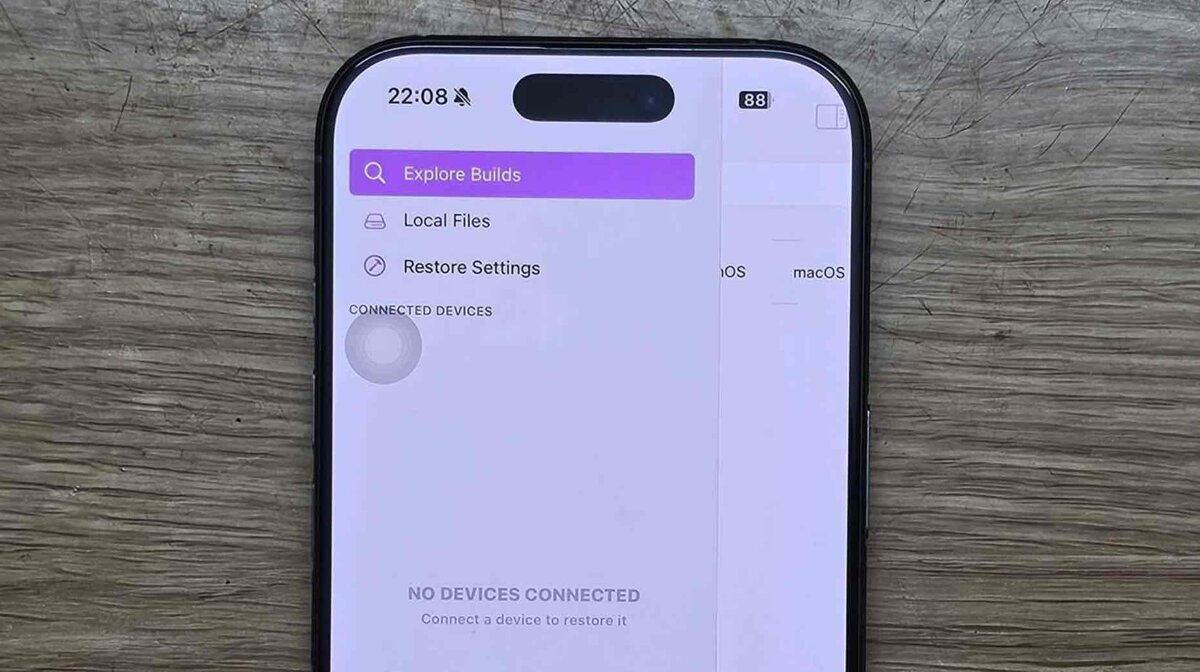 木目のテーブルの上に置かれたiPhoneの画面に、開発者向けツール「PurpleRestore 4」のモバイル版と思われるUIが表示され、ビルド探索・ローカルファイル・復元設定などの項目が並んでいる様子