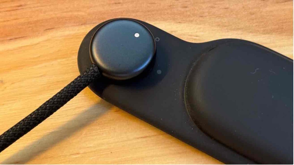 木目のテーブルの上に置かれた、編み込みの黒いケーブルがつながった円形の黒いコネクタ部品とバンド一体型モジュールのクローズアップ写真