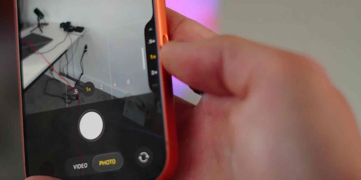 iPhoneのカメラ操作を示すイメージ。側面のカメラコントロールボタンを指で操作しながら、画面上でズーム倍率を調整している様子。