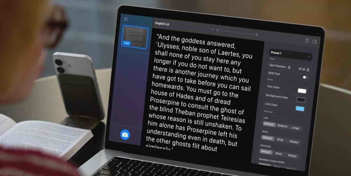 Macの画面に表示された英文テキストを拡大表示するアクセシビリティ機能の使用イメージ。横にiPhoneと書籍が置かれている