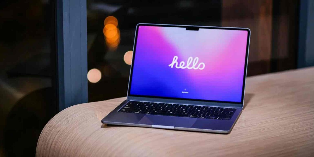 夜の室内でテーブルに置かれたMacBook。ディスプレイには「hello」と表示され、薄型デザインとキーボードが確認できる。