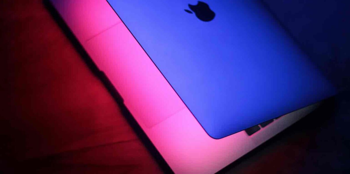 MacBookの天板(Appleロゴ)を、ピンクとブルーのネオン光で斜めから照らしたクローズアップ写真