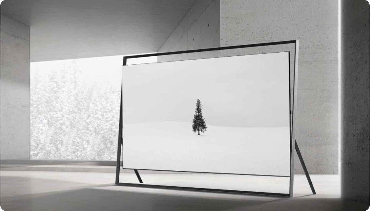 コンクリート調の室内空間に設置された大型テレビが、雪原に一本の木が立つミニマルな映像を表示している様子