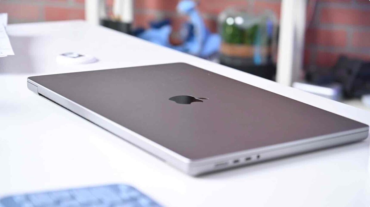 MacBookを閉じた状態で白いデスク上に置いたクローズアップ。天板のAppleロゴが見え、背景は室内がぼかされている