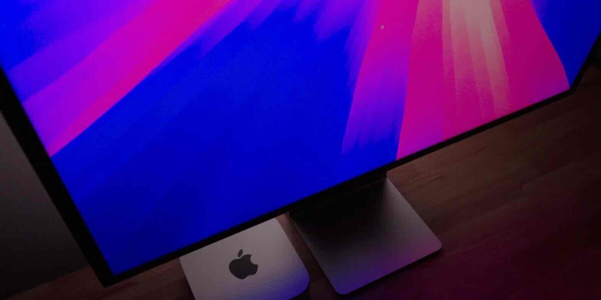 紫と青のグラデーション壁紙を表示したAppleの外部ディスプレイ。金属製スタンドとAppleロゴが見える下部ベゼルのクローズアップ