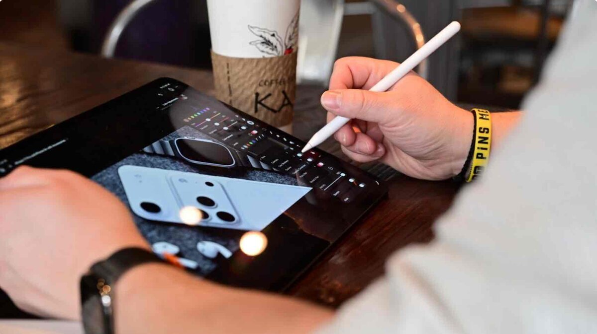カフェのテーブルでiPadとApple Pencilを使い、Pixelmator Proで写真を編集している様子。iPhoneの背面デザインを調整している画面が表示されている