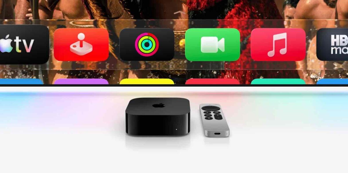 黒い筐体のApple TV 4K本体と、シルバーのSiri Remote。背景にはtvOSのホーム画面がボケて写っており、Apple TVアプリやミュージック、設定などのアイコンが並んでいる