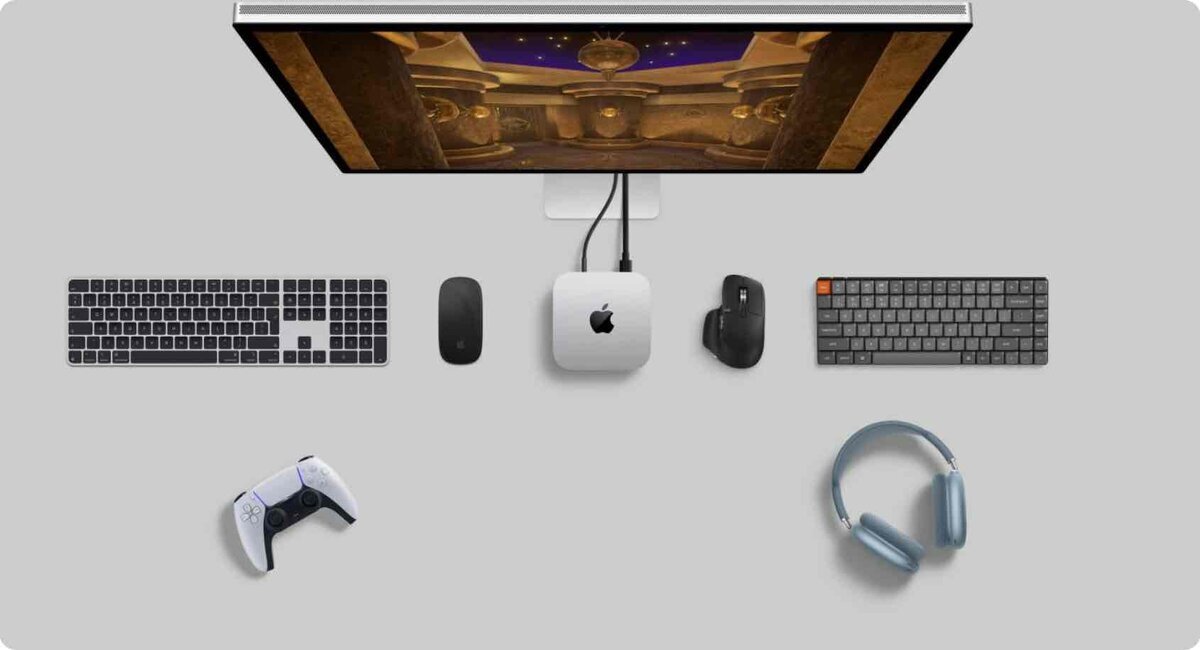 グレーの背景に、最新のM4 Mac miniを中心としたガジェットの俯瞰写真。中央上部にはモニターがあり、Mac mini本体と接続されている。その周囲を囲むように、左側にはApple純正のMagic Keyboard(テンキー付き)とMagic Mouse、右側にはLogicool(Logitech)のMX Master 3マウスとメカニカルキーボード、さらに下部にはPlayStation 5のDualSenseコントローラーとAirPods Max(スカイブルー)が左右対称に近いレイアウトで配置されている